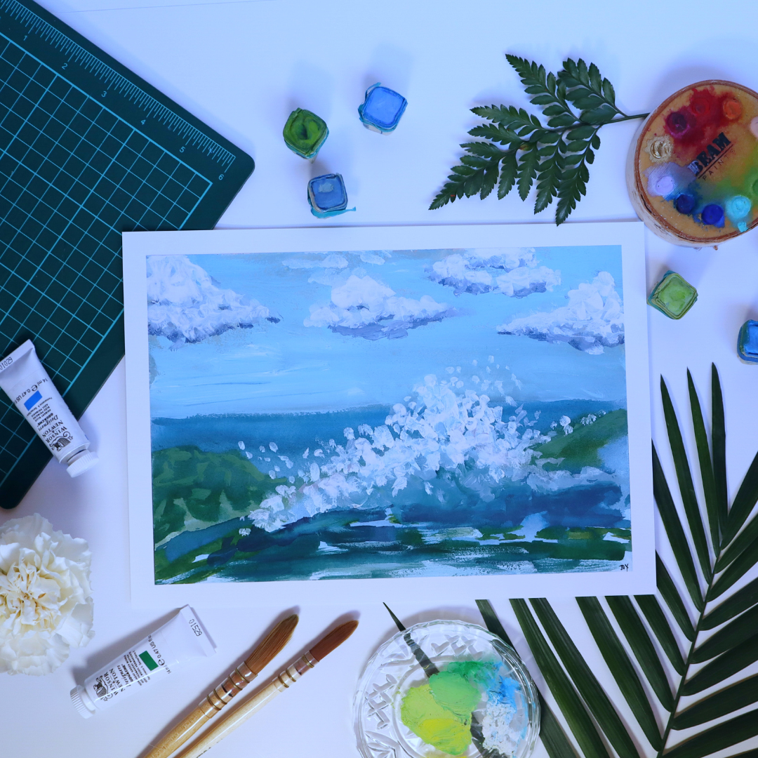 Painting of "splash" abstract of waves coming in with cloudy sky, painting surrounded by art supplies like watercolour palettes, paint brushes, greenery, flowers